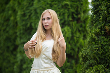 Portrait of a young pretty blonde girl in a dress between thuja on the street in autumn.