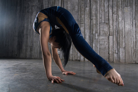 Young extremely flexible female acrobat standing on hand over gray background in photo studio - Powered by Adobe