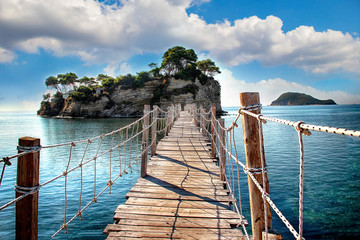 The wooden bridge overlooking the sea leads to an island with palm trees. It's a rope bridge. It is...