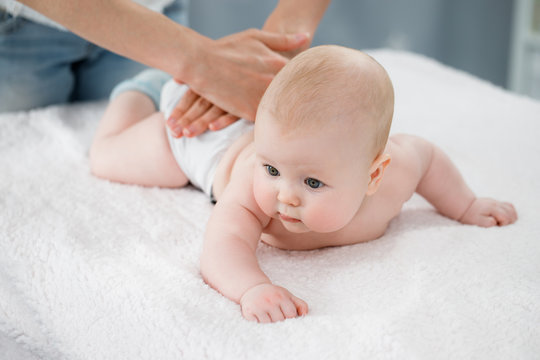 Mother's hands massage the muscles of the back of her baby. Preventive gymnastics. Light background