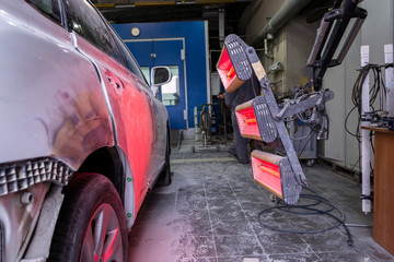 Infrared drying of car body parts after applying putty and paint on a white off-road vehicle in the body repair shop with red lanterns in the working environment