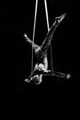 Circus artist on the aerial straps making cross with strong muscles on black background
