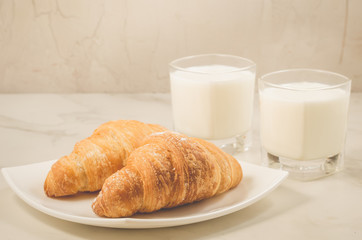 breakfast with croissants and milk/croissants in a white plate and two glasses milk on a marble background. Selective focus