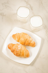breakfast with croissants and milk/croissants in a white plate and two glasses milk on a marble background. Top view