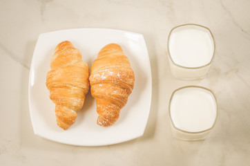 croissants in a white plate and two glasses milk/croissants in a white plate and two glasses milk on a white background. Top view