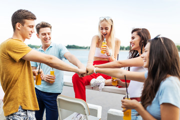 A company of good-looking friends laughing and drinking yellow cocktails and socialising in the nice cafe next to the river. Cheers. Entertainment, having good time. River is in the background.