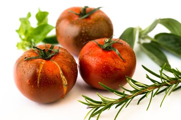 Three dark tomato with green herb leaf.