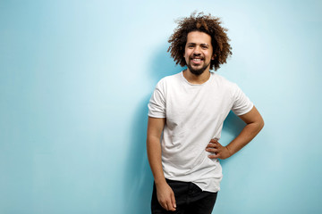 Fototapeta na wymiar Smiling curly-headed man in white T-shirt with a hand on the hip. An easy going person with positive outlook. Happiness and joy in the eyes.