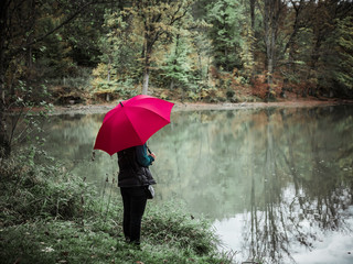 Woman with red umbrella stands next to a lake