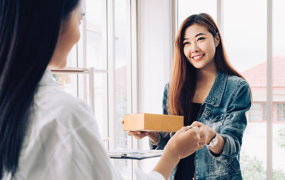 Customer order product packaging concept. Two young Asian woman smiling happy with checking customers order list in modern home office with brown package box in hands