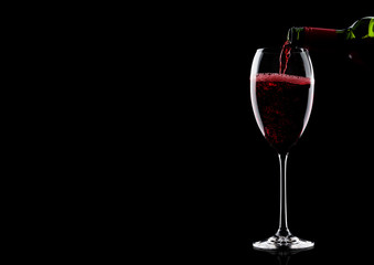 Pouring red wine from bottle to glass on black with space for your text