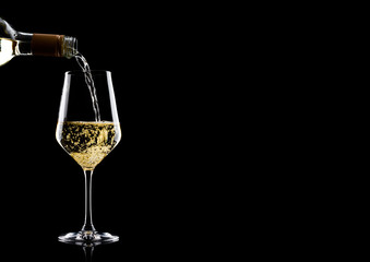 Pouring white wine from bottle to glass on black with space for your text