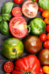 various colorful tomatoes and basil leaves on rustic table.