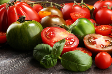 various colorful tomatoes and basil leaves on rustic table.