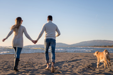 couple with dog having fun on beach on autmun day