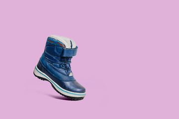 A small blue shoe isolated on a pink, pastel background. Shoes on a blue background. Warm, fur-lined baby velcro shoes. Concept of the coming autumn and winter.