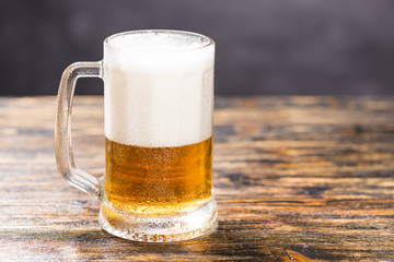 Cold glass of lager beer with foam and dew on dark background with copy space