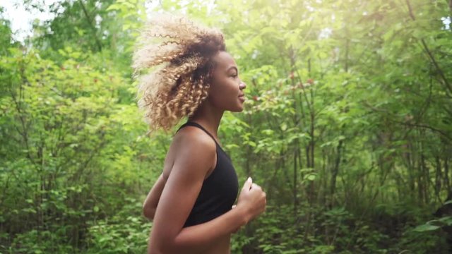 young beautiful African American woman with curly hair running in a forest, close up
