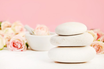 Fototapeta na wymiar White spa stones on table set with roses and pink background, relaxing aromatherapy. 