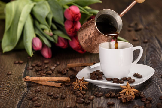 Pouring coffee into a white cup against the background of tulips close up