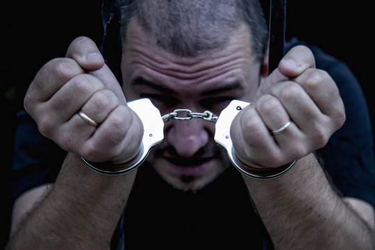 Portrait of handcuffed criminal man imprisoned.