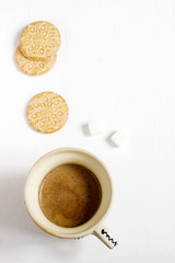 Coffee with milk in an old cup, served with biscuits and sugar on a light background.