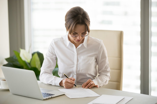 Serious successful businesswoman puts signature on business contract, millennial female entrepreneur signing paper doing paperwork at workplace, woman boss working with documents in office