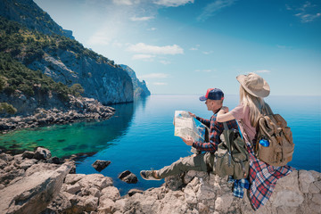 Couple Travelers Man and Woman with a map sitting relax in a hike. Hikers with backpacks in the mountains by the sea. Young family traveling active adventure.