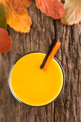 Fresh homemade pumpkin smoothie in glass with drinking straws, photographed overhead on wood with colorful autumn leaves  (Selective Focus, Focus on the drink)