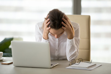 Frustrated stressed businesswoman holding head in hands shocked by bankruptcy or business failure...