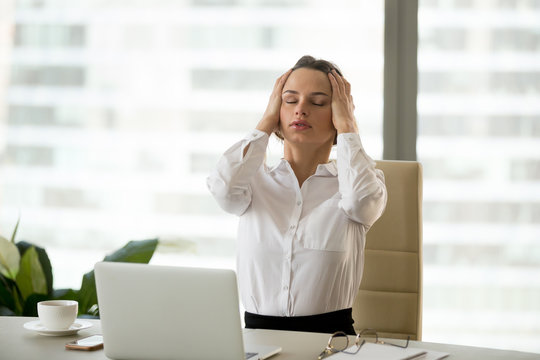 Stressed exhausted businesswoman having strong headache at work holding head in hands, frustrated overwhelmed office worker suffering from aching head feeling pressure or migraine tired of overwork