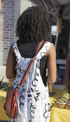 Back view of unrecognizable African American girl in a cute dress with purse standing at a honey vendors stall at a farmers market