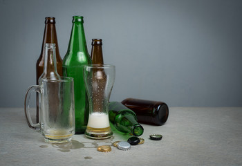 Empty beer glass with bottle caps and bottles on grey concrete,after party