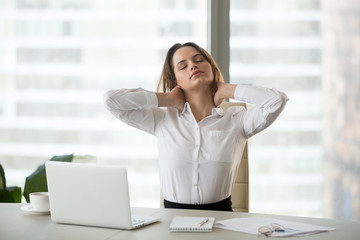 Young businesswoman touching massaging stiff neck after sedentary computer work in incorrect posture, fatigued employee taking work break for doing easy office exercises to relieve pain in muscles