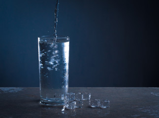Ice splashes into glass of water on blue background