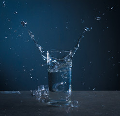 Ice splashes into glass of water on blue background