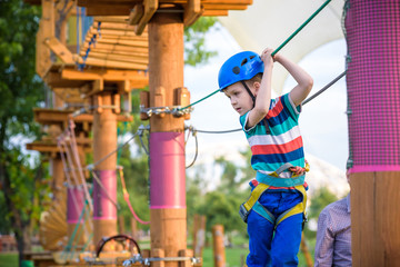 Little cute boy enjoying activity in a climbing adventure park on a summer sunny day. toddler climbing in a rope playground structure.