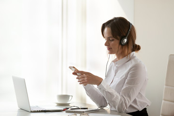 Smiling businesswoman in headphones holding phone listening music in smartphone player online at...