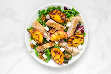 Chicken salad with grilled peach, mixed salad, feta cheese and walnuts in a plate. healthy food