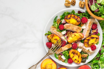 vitamin salad with grilled chicken and peach, feta cheese, raspberries and walnuts in a plate....