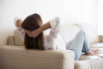 Obraz premium Rear view at relaxed lazy woman resting on comfortable couch sofa feeling mental balance, dreaming of satisfaction, breathing fresh air, enjoying no stress free peaceful calm weekend morning at home