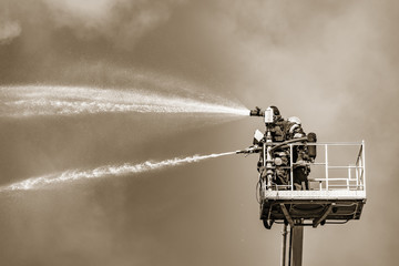 Firefighters extinguish a fire by the top of the building.