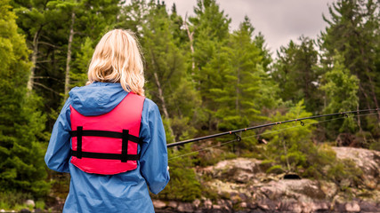 A young girl with blond hair is fishing in a lake