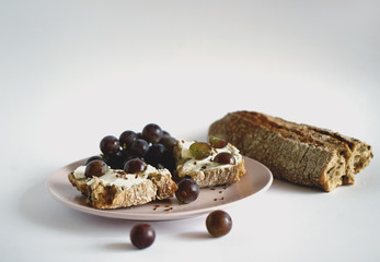 Sandwich of buckwheat bread with cream cheese and grapes with flax seeds on a pink plate