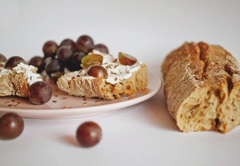 Sandwich of buckwheat bread with cream cheese and grapes with flax seeds on a pink plate
