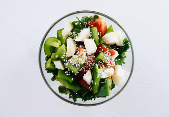 Salad of pepper, tomato, olives, cheese and sesame in a glass plate on a white background