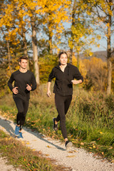 Fototapeta premium Young veautiful couple runs on a path in park on autumn afternoon