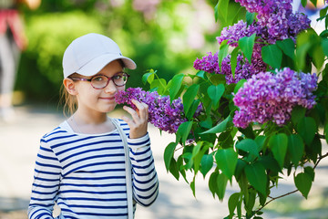 Smiling baby girl and lilac bush in the garden. Selective focus.