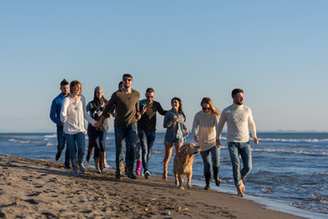 Group of friends running on beach during autumn day