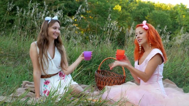 Cheerful young women siting at the meadow picnic and has a rest with drink 